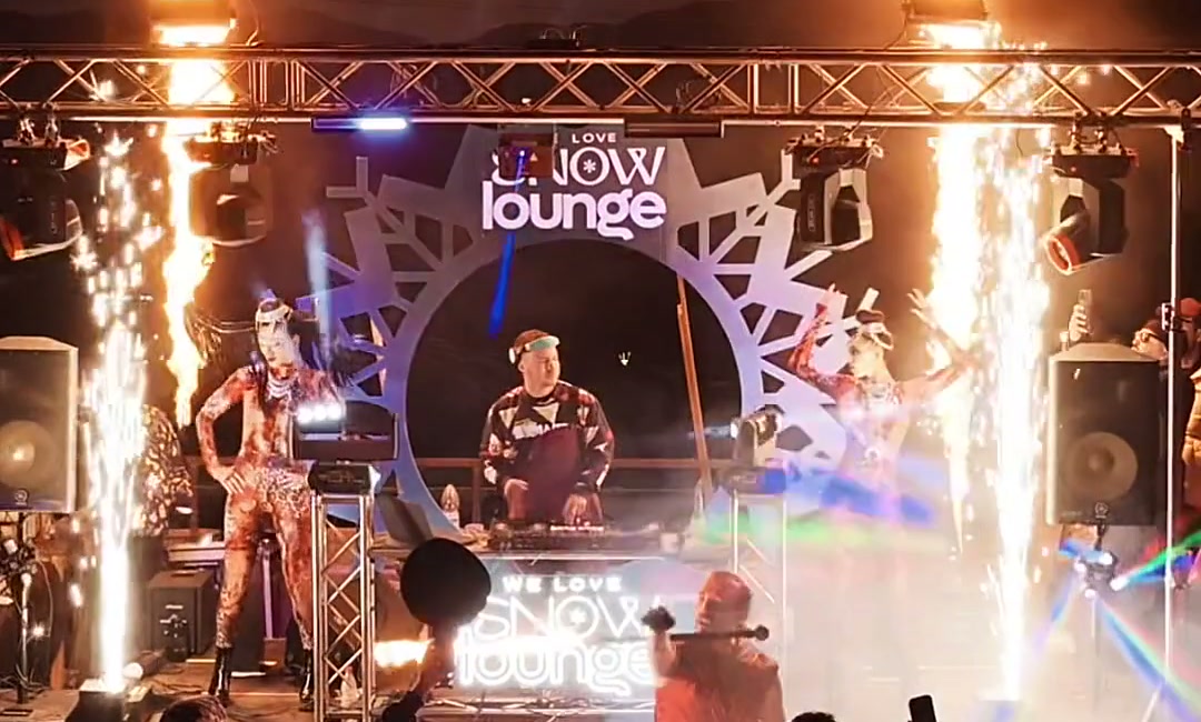 Performer fazendo show de fogo com tochas na We Love Snow Lounge ao entardecer.