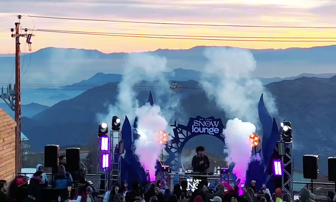 DJ tocando com fumaça e luzes na pista da We Love Snow Lounge ao pôr do sol.
